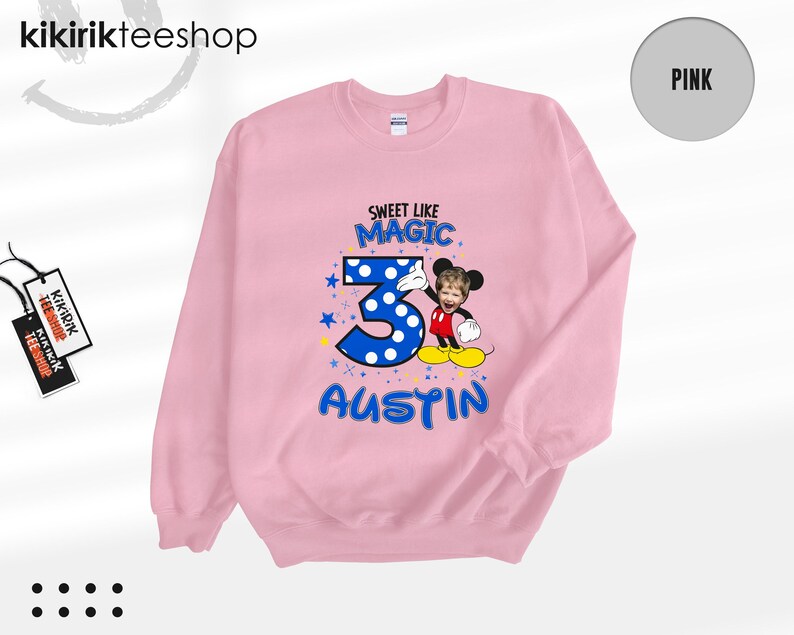 May include: A light pink long-sleeve sweatshirt featuring a graphic print with the text "SWEET LIKE MAGIC", a large blue polka-dot number "3", and the name "AUSTIN" in blue. A cartoon character with a child's face is positioned next to the number.