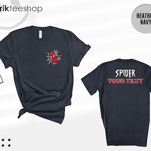 May include: A heather navy short-sleeve t-shirt featuring a small red spider-themed character graphic on the front left chest and the text "SPIDER YOUR TEXT" printed in white and red on the back. The shirt includes a branded tag attached.