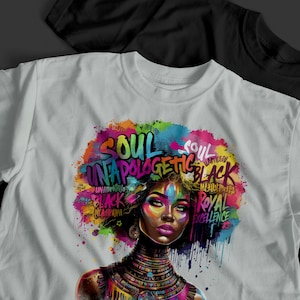 May include: White t-shirt featuring a colorful graphic of a woman with the words "SOUL UNAPOLOGETIC BLACK" and "ROYAL EXCELLENCE". The design incorporates vibrant hues of blue, pink, yellow, and green. A black t-shirt is visible in the background.