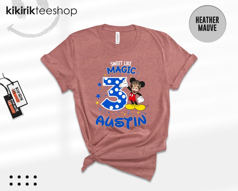 May include: A heather mauve t-shirt featuring a graphic with the text "SWEET LIKE MAGIC" above a large blue polka-dot number 3, a cartoon character with a child's face, and the name "AUSTIN" in blue letters, accented with small yellow stars.
