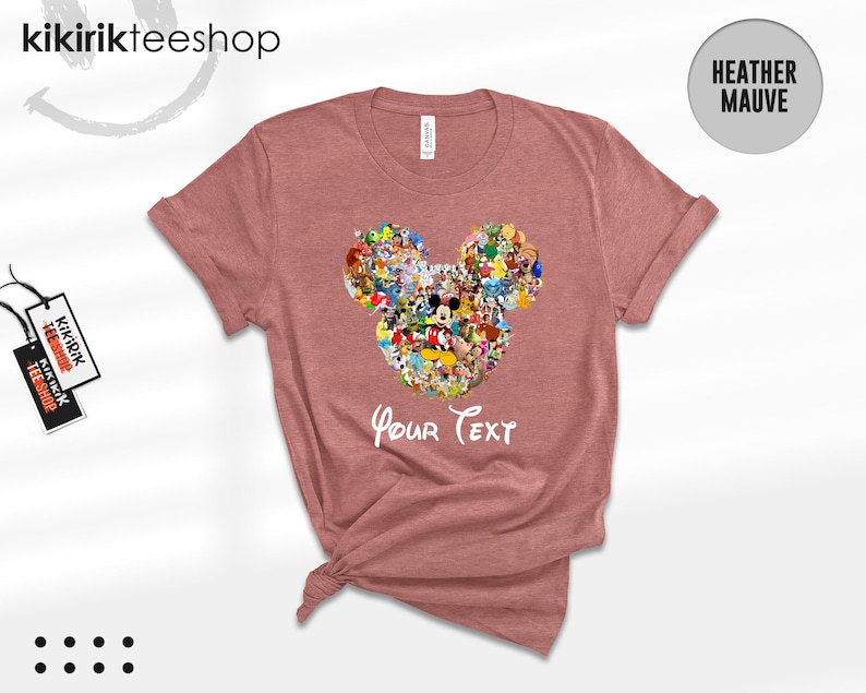 Pu&ograve; includere: T-shirt color malva con un design a forma di testa di Topolino riempita con vari personaggi dei cartoni animati. Le parole "Your Text" sono stampate sotto il disegno. La maglietta ha maniche corte e girocollo.