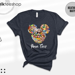 Pu&ograve; includere: T-shirt blu navy melange con un design a forma di testa di Topolino composto da vari personaggi dei cartoni animati. Le parole "Your Text" sono scritte in bianco sotto il disegno. La maglietta ha le maniche arrotolate e l'orlo annodato.
