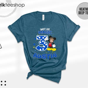 May include: A heather deep teal t-shirt featuring a graphic with the text "SWEET LIKE MAGIC" above a large blue polka-dot number "3" and the name "AUSTIN" below. A cartoon character with a child's face is positioned next to the number.