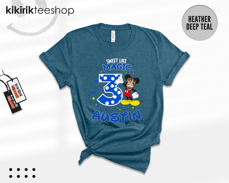 May include: A heather deep teal t-shirt featuring a graphic with the text "SWEET LIKE MAGIC" above a large blue polka-dot number "3" and the name "AUSTIN" below. A cartoon character with a child's face is positioned next to the number.
