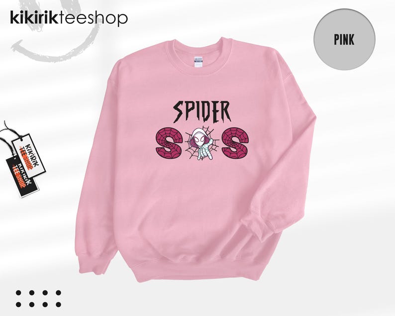 May include: A light pink crewneck sweatshirt featuring a graphic print on the chest. The design includes the text SPIDER above the letters S, O, and S, which are filled with a red spiderweb pattern. A small white spider character is centered.