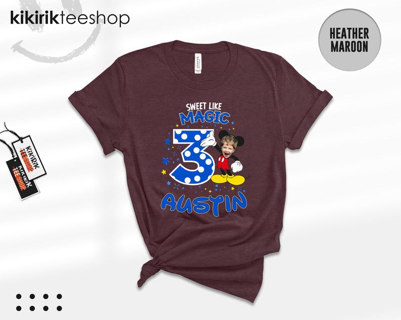 May include: A heather maroon short-sleeve t-shirt featuring a graphic with the text SWEET LIKE MAGIC, the number 3 in blue with white polka dots, and the name AUSTIN. A cartoon character body with a child's face is positioned next to the number 3.