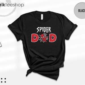 May include: A black short-sleeve t-shirt featuring the white text SPIDER above the word DAD. The letter A is replaced by a red and black spider-themed character centered within a white spiderweb graphic. The shirt has a crew neckline.