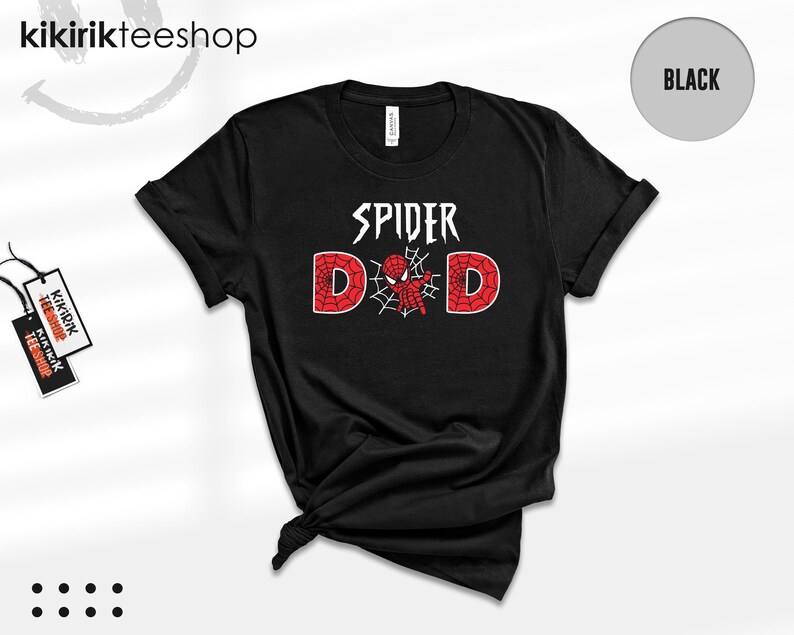 May include: A black short-sleeve t-shirt featuring the white text SPIDER above the word DAD. The letter A is replaced by a red and black spider-themed character centered within a white spiderweb graphic. The shirt has a crew neckline.