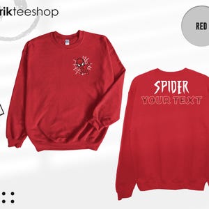 May include: A red long-sleeve sweatshirt featuring a small graphic of a spider-themed character on a web on the left chest. The back displays the white text SPIDER and the outlined text YOUR TEXT. Includes a tag labeled kikirikteeshop.