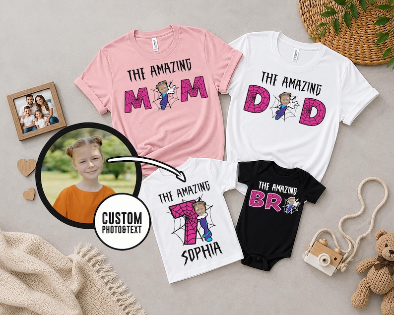 May include: A collection of four garments including a pink t-shirt with text THE AMAZING MOM, a white t-shirt with text THE AMAZING DAD, a white t-shirt with text THE AMAZING SOPHIA, and a black bodysuit with text THE AMAZING BRO, all featuring spiderweb graphics.