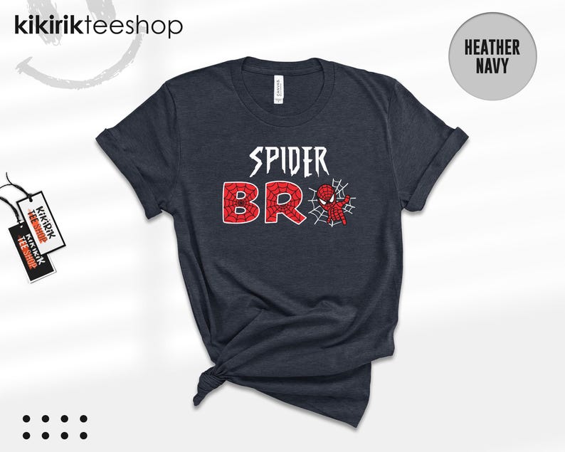 May include: A heather navy short-sleeve t-shirt featuring the white text SPIDER above the red text BRO, with a small red and blue spider-themed character and a white spiderweb graphic integrated into the letter O on the front of the garment.