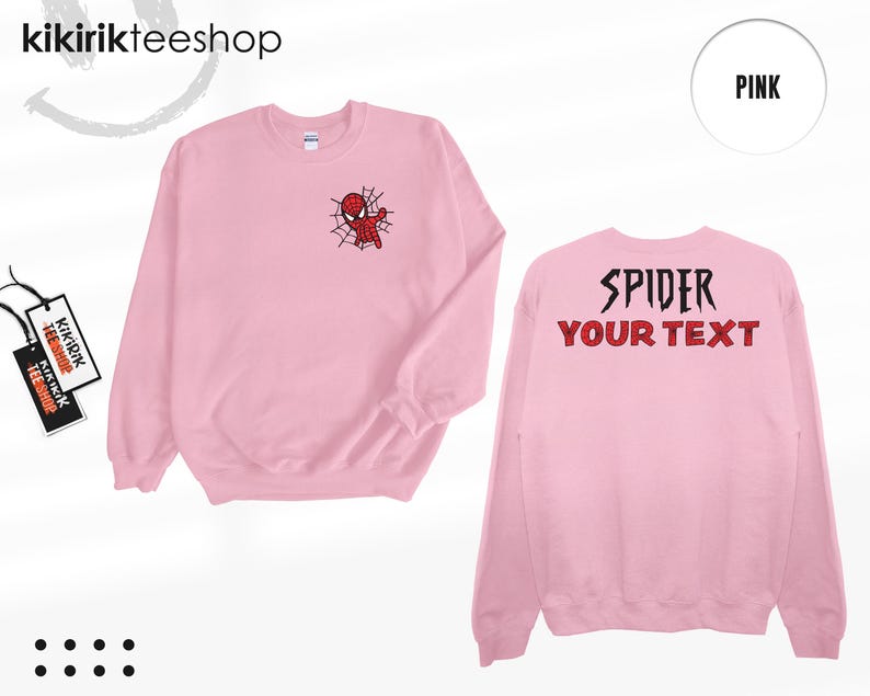May include: A light pink crewneck sweatshirt featuring a small graphic of a red spider-themed character on a web on the left chest. The back displays the black text SPIDER and the red text YOUR TEXT. A tag with the text KIKIRIKTEESHOP is attached.