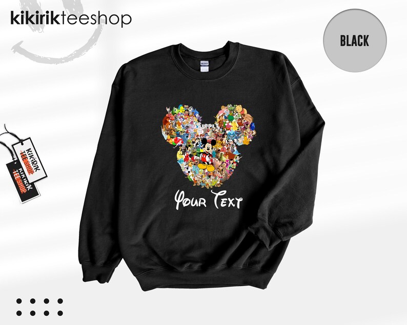 Pu&ograve; includere: Felpa girocollo nera con un colorato design a forma di testa di Topolino composto da vari personaggi dei cartoni animati. Le parole "Your Text" sono scritte in bianco sotto. La felpa ha un'etichetta con scritto "Kikirik Tees Shop".