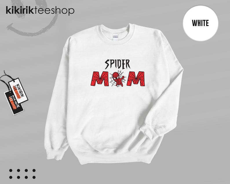 Puede incluir: Sudadera blanca con el texto "SPIDER MOM" en negro y rojo. El dise&ntilde;o presenta una telara&ntilde;a y una ara&ntilde;a de dibujos animados. La sudadera tiene cuello redondo y mangas largas. La marca "kikirikteeshop" es visible en la esquina superior izquierda.