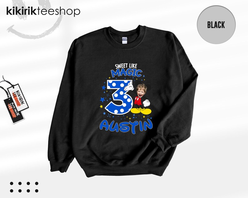 May include: A black long-sleeve sweatshirt featuring a graphic print with the text "SWEET LIKE MAGIC" above a large blue polka-dot number three, the name "AUSTIN" below, and a cartoon character body with a child's face and yellow shoes.
