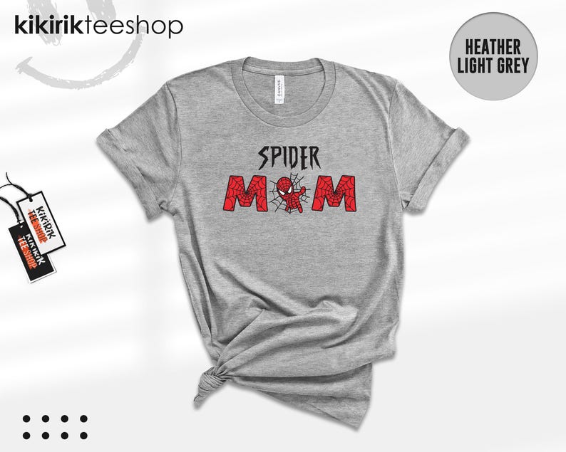 Puede incluir: Camiseta gris jaspeado claro con las palabras "SPIDER MOM" en negro y rojo. El dise&ntilde;o incluye un gr&aacute;fico de ara&ntilde;a. La camiseta est&aacute; anudada en la parte inferior. La marca "kikirikteeshop" es visible en la parte superior izquierda.