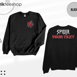May include: A black long-sleeve sweatshirt featuring a small red and white spider-themed graphic on the left chest. The back of the sweatshirt displays the white text SPIDER above the red text YOUR TEXT in a stylized font. Includes brand tags.