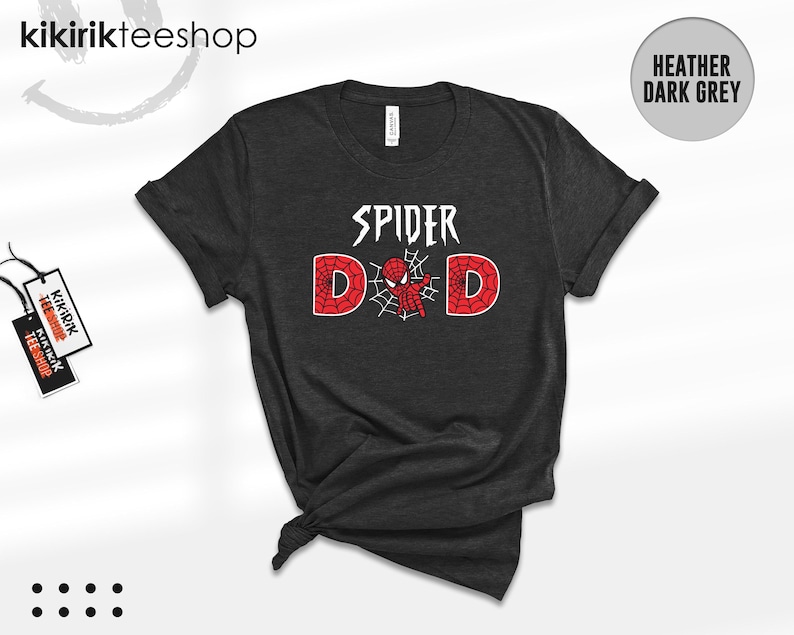 Puede incluir: Camiseta gris oscuro jaspeado con el texto "SPIDER DAD" en blanco y rojo. El dise&ntilde;o incluye un gr&aacute;fico de Spider-Man. La camiseta est&aacute; doblada en la parte inferior y tiene una etiqueta.