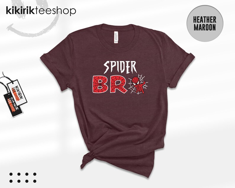 May include: A heather maroon short-sleeve t-shirt featuring the white text SPIDER above the red web-patterned text BRO, with a small red and blue spider-themed character graphic positioned next to the letter O and a white spider web design.