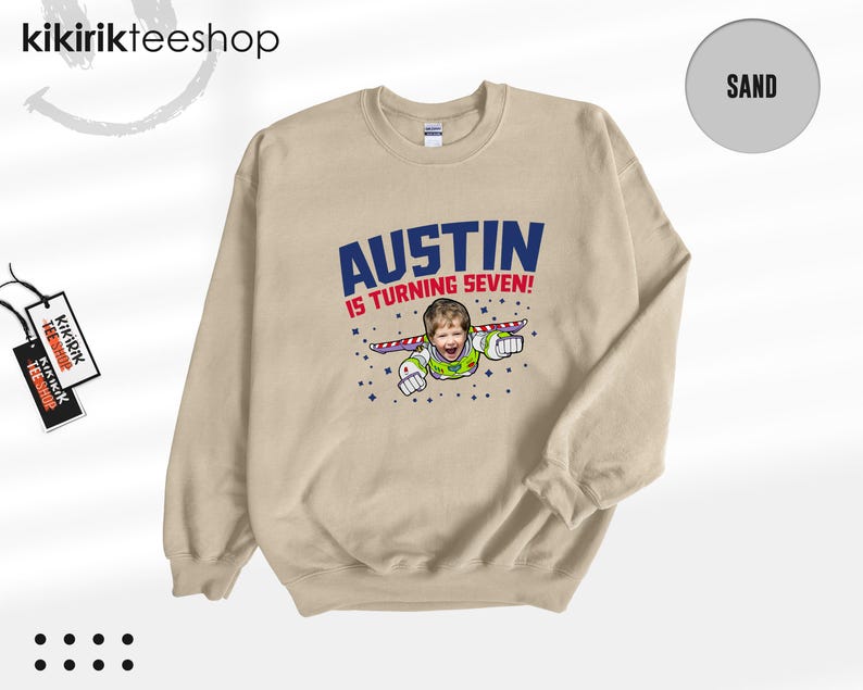K&ouml;nnte beinhalten: Ein sandfarbenes Sweatshirt mit Rundhalsausschnitt und einem Grafikdruck, der das Gesicht eines Kindes auf dem K&ouml;rper eines Weltraum-Rangers zeigt. Der Text AUSTIN IS TURNING SEVEN! ist in blauen und roten Buchstaben mit Sternen abgebildet.