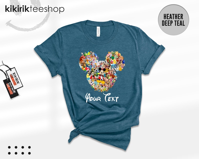 Pu&ograve; includere: T-shirt color teal melange con un design a forma di testa di Topolino composto da vari personaggi dei cartoni animati. Le parole "Your Text" sono scritte in bianco sotto il disegno. La maglietta &egrave; piegata e annodata in basso.