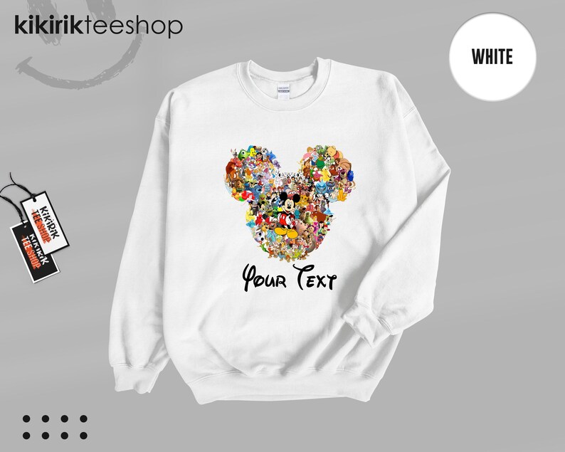 Pu&ograve; includere: Felpa bianca con un colorato design a forma di testa di Topolino composto da vari personaggi dei cartoni animati. Le parole "Your Text" sono scritte in un carattere script sotto il design. La felpa ha un girocollo.