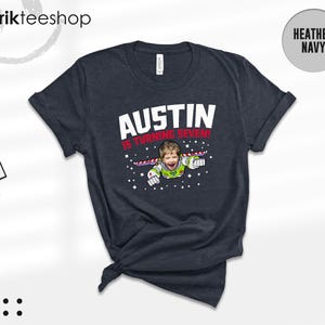 K&ouml;nnte beinhalten: Ein kurz&auml;rmeliges T-Shirt in Heather Navy mit einer Grafik eines Kindes in einem Weltraum-Ranger-Kost&uuml;m, das vor einem Sternenhintergrund fliegt. Der Text AUSTIN IS TURNING SEVEN! ist in Wei&szlig; und Rot gedruckt. Mit Rundhalsausschnitt.