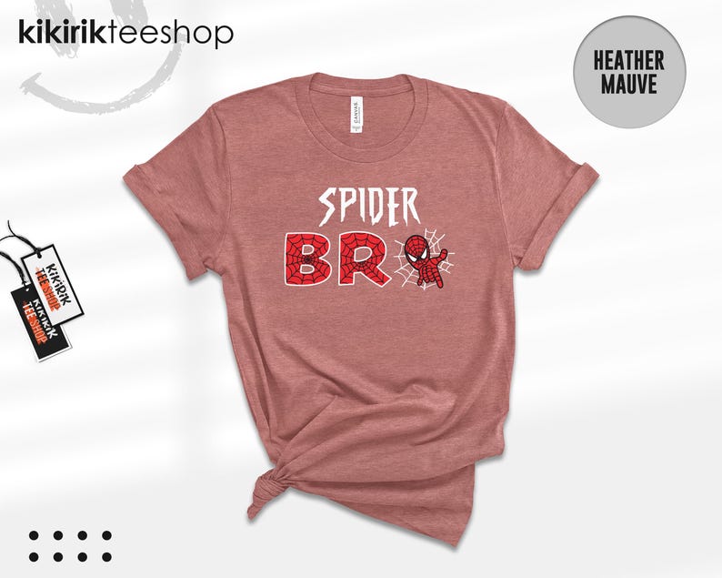 May include: A heather mauve short-sleeve t-shirt featuring the white text SPIDER and the red web-patterned text BRO, accompanied by a small red and blue spider-themed character graphic and a white spider web design on the front center.