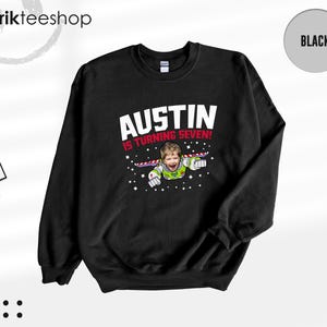 K&ouml;nnte beinhalten: Ein schwarzes Langarm-Sweatshirt mit einem Grafikdruck, der das Gesicht eines Kindes auf dem K&ouml;rper einer Weltraum-Ranger-Figur zeigt. Der Text AUSTIN IS TURNING SEVEN! ist in wei&szlig;er und roter Schrift mit kleinen Sternen abgebildet.