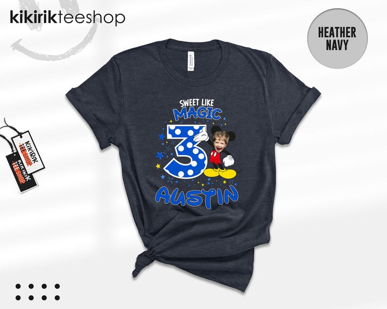 May include: A heather navy short-sleeve t-shirt featuring a graphic with the text "SWEET LIKE MAGIC" above a large blue polka-dot number "3" and the name "AUSTIN" below. A cartoon character with a child's face is positioned next to the number.