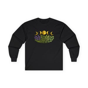Könnte beinhalten: Ein schwarzes Langarmshirt mit einer zentralen Grafik eines goldenen Mondzyklus über einer Ansammlung grüner botanischer Elemente, darunter Lavendelzweige, Rosmarin und verschiedene Blätter, alles in einem detaillierten Illustrationsstil.