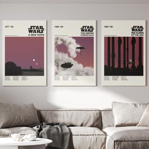 May include: Three vintage Star Wars movie posters with a minimalist design. The posters are framed and hanging on a white wall above a beige sofa. The posters feature the titles "Star Wars: A New Hope", "Star Wars: The Empire Strikes Back", and "Star Wars: Return of the Jedi".
