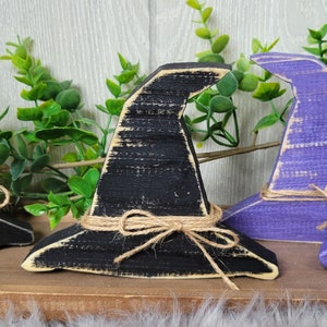 May include: A black wooden witch hat with a brown twine bow. The hat is distressed and has a rustic look.