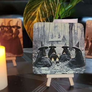 Puede incluir: Piezas de arte de madera con im&aacute;genes vintage de brujas con sombreros puntiagudos. Una muestra brujas en un bosque, otra representa un grupo de brujas de pie juntas. Velas encendidas en primer plano crean un ambiente m&iacute;stico.