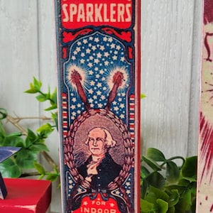May include: Vintage-style wooden sign with a red, white, and blue design. The sign features a portrait of George Washington and the text "Leader Sparklers" and "For Indoor and Outdoor Illuminations. Don't Touch. The Glowing Wire. Mfd. By Acme Sparkler and Specialty River Grove Ill. Made in USA Essex Brand."