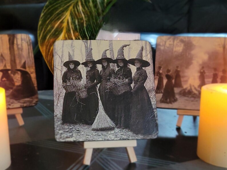 Puede incluir: Posavasos cuadrado con una imagen vintage en blanco y negro de cinco mujeres con sombreros de bruja y vestidos largos, sosteniendo cestas y una escoba. La imagen est&aacute; ambientada en un fondo de bosque, evocando un tema de Halloween o g&oacute;tico.