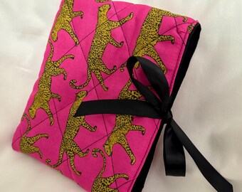 May include: A pink quilted pouch with a black ribbon closure. The pouch is decorated with a repeating pattern of yellow leopards on a pink background.