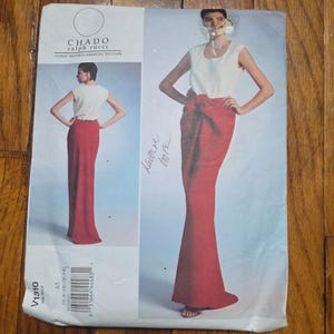 May include: A vintage sewing pattern by Chado Ralph Rucci. The pattern features a sleeveless white top paired with a long, red skirt. The pattern number is V1310, and the size range is 6-14.