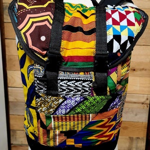 May include: A colorful patchwork backpack with a variety of African-inspired fabric patterns. The backpack features black straps, buckles, and a flap closure. The design includes geometric shapes, floral motifs, and vibrant colors.