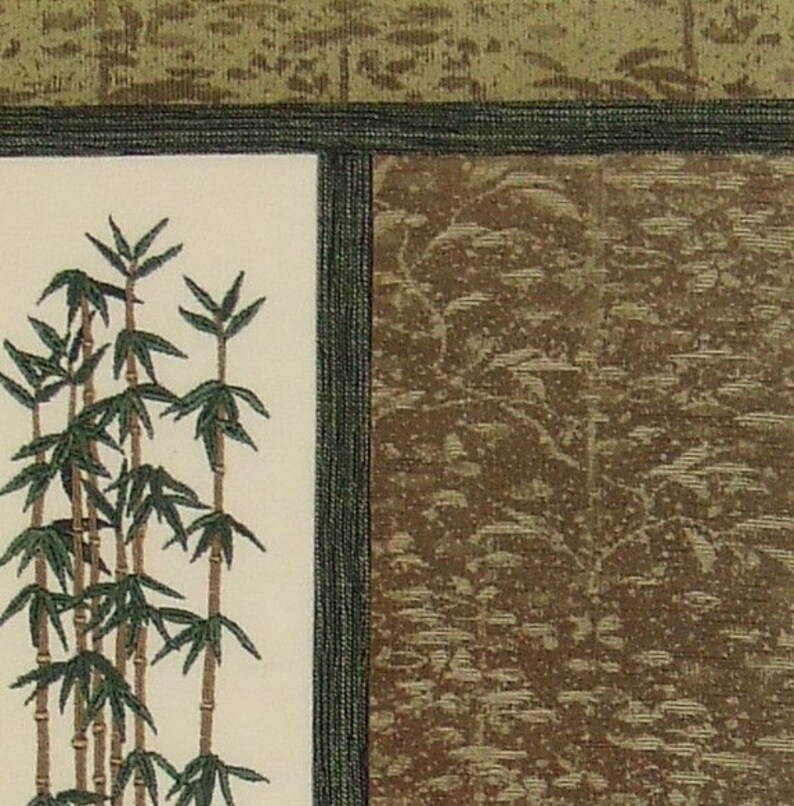 May include: A close-up of a cream-coloured fabric with an embroidered design of green bamboo stalks. The fabric is framed by a dark green border.