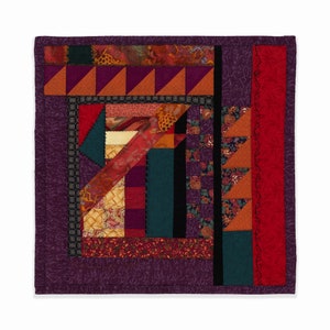 May include: A purple quilted wall hanging with a geometric design made from various fabrics in shades of red, orange, brown, green, and black.