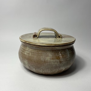 May include: A ceramic lidded jar with a brown and white glaze. The jar has a rounded body and a lid with a handle.
