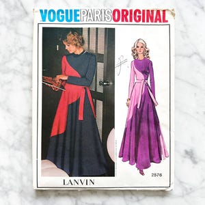 Könnte beinhalten: Vintage Vogue Paris Original Schnittmuster für ein Kleid von Lanvin. Die Schnittmuster-Nummer lautet 2576. Das Schnittmuster zeigt zwei Models, die ein langes Wickelkleid mit einem kontrastierenden Farbfeld tragen. Ein Model trägt ein schwarz-rotes Kleid, das andere ein violettes Kleid.