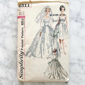 May include: Vintage Simplicity printed pattern 4511 for wedding dresses. The pattern features illustrations of three different bridal gown designs, including a long-sleeved gown with a veil, a short dress, and a gown with a full skirt. The pattern size is 14, bust 86 cm.