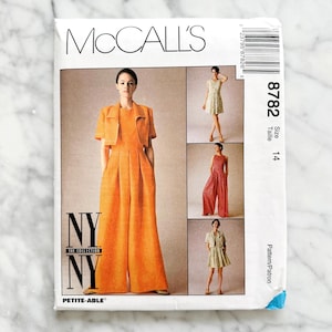 May include: A McCall's sewing pattern featuring a woman in an orange jumpsuit and jacket. The pattern includes multiple garment options, with the text "NY THE COLLECTION" and "PETITE-ABLE". The pattern size is 14.