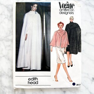 May include: A vintage Vogue American Designers sewing pattern featuring a woman in a white cape and illustrations of cape designs. The pattern includes the text "edith head" and the number "2617".