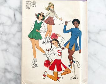 Simplicity 8131 – Niñas 7 y 8. Uniforme de animadora de los años 70, con minivestido, falda y pantalones cortos de skater. Patrón de costura vintage.
