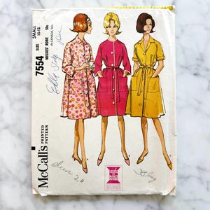 May include: Vintage McCall's sewing pattern 7554 for Misses' robes. The pattern features illustrations of three robe designs in pink floral, fuchsia, and yellow. The pattern size is small, 10-12. The price is 50 cents.