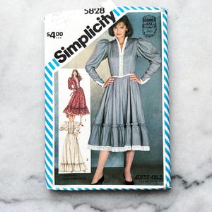 May include: Simplicity sewing pattern number 5828 for a dress with a lace trim and puff sleeves. The pattern is for misses sizes and is adjustable. The pattern cover features a model wearing a blue dress with white lace trim and a white blouse underneath.