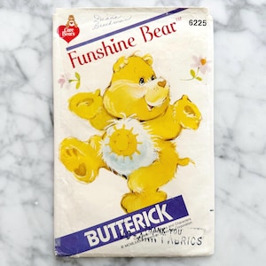 Puede incluir: Un patr&oacute;n de costura Butterick vintage con Funshine Bear de Care Bears. La portada del patr&oacute;n es blanca con una ilustraci&oacute;n de Funshine Bear amarillo. El texto incluye "Funshine Bear" y "Butterick". El n&uacute;mero de patr&oacute;n es 6225.